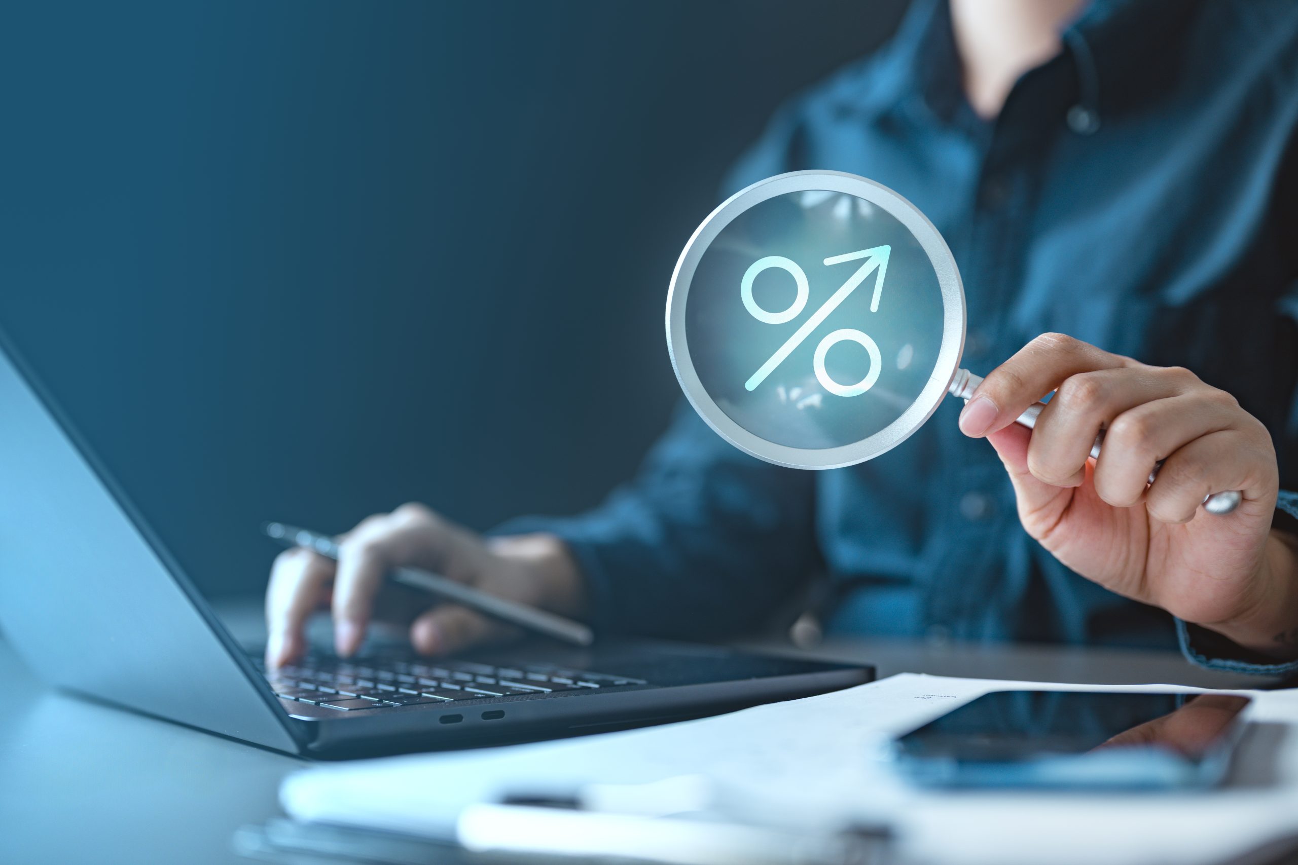 person holding magnifying glass analyzing numbers at a computer